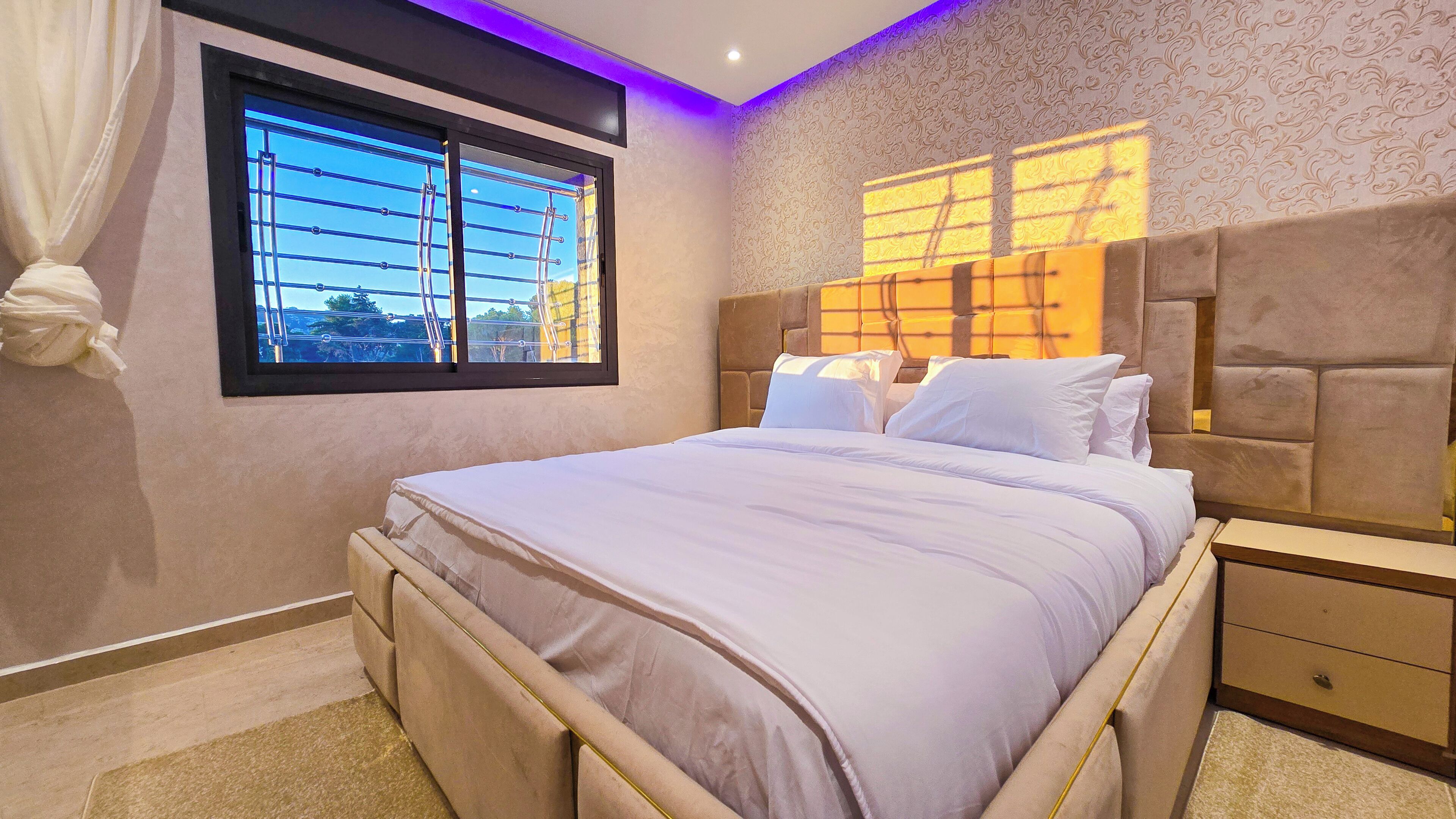 A bedroom with a bed, bedside tables, a window with blinds, and a patterned wall.
