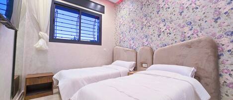 A bedroom with two beds, a window with blinds, a floral wallpaper, and a red light strip on the ceiling.