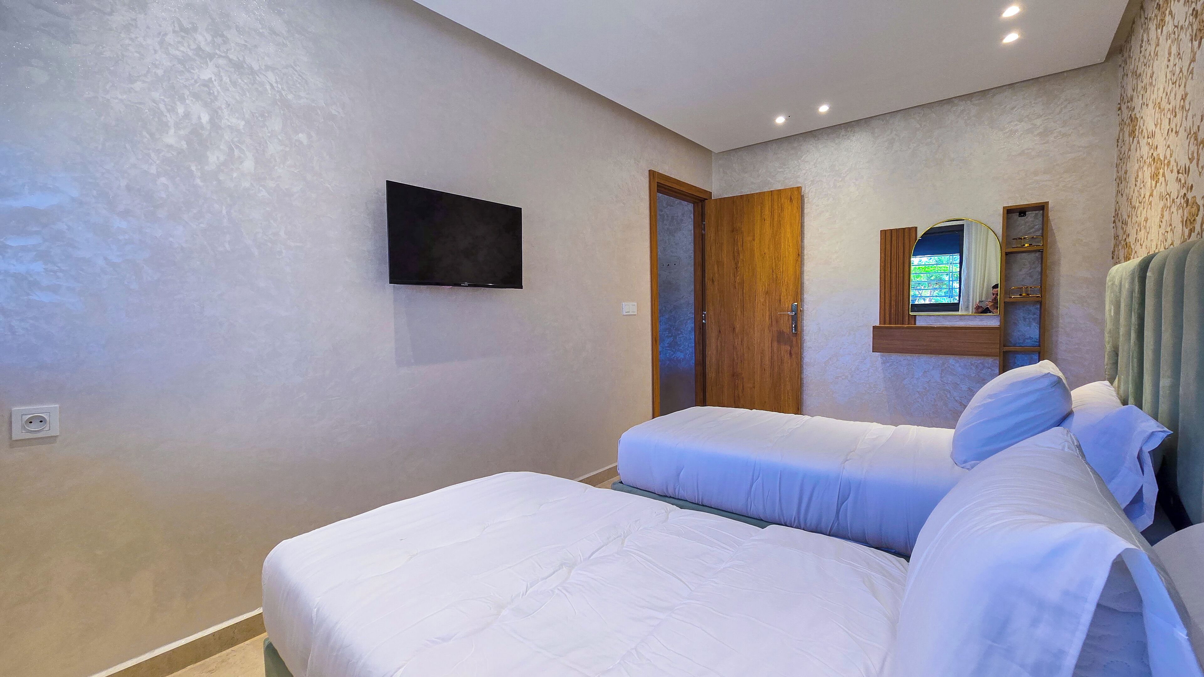 A bedroom with two beds, a TV mounted on the wall, and a wooden door.