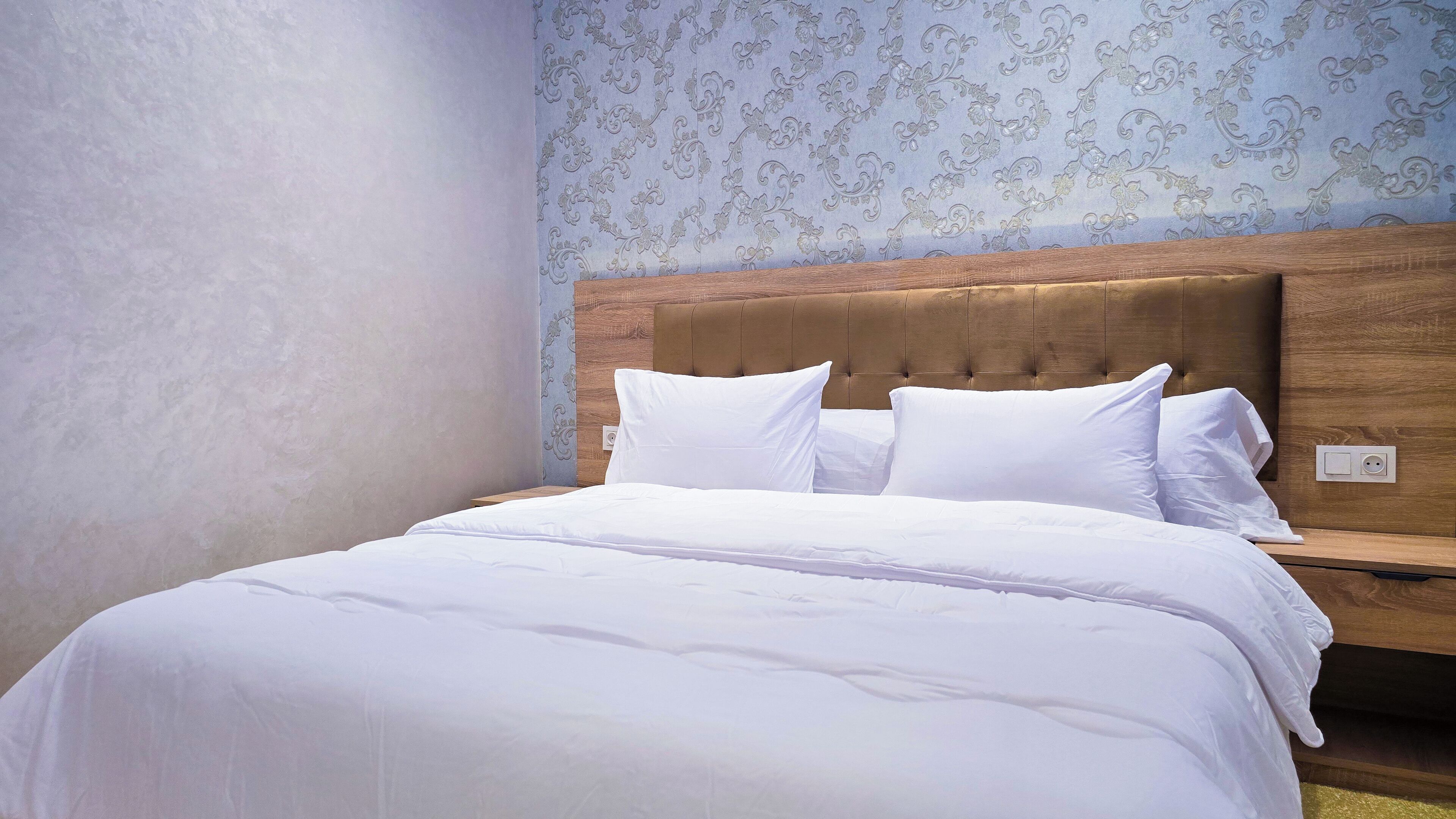 Una cama bien hecha con ropa blanca en una habitación con cabecera de madera y papel tapiz estampado.