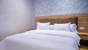 Una cama bien hecha con ropa blanca en una habitación con cabecera de madera y papel tapiz estampado.