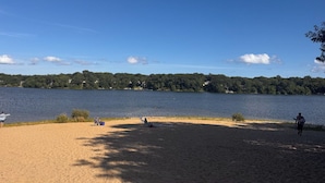 Een strand met een heldere lucht, kalm water en een verre kustlijn met bomen.