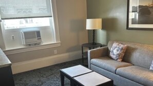 A living room with a grey sofa, a small table, a lamp, and a window with blinds. - Sep 29- Oct 2, Historic Hotel 10 mins from AI Conference 2026, SF 1BR/2BA, (San Francisco)