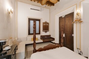 Un dormitorio con una cama grande, un aparador de madera, un banco, un espejo montado en la pared y una puerta con perchero.