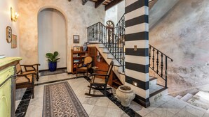A spacious lobby with a marble floor, a wooden reception desk, a large potted plant, a rocking chair, and a staircase with black and white striped walls. - Casa Lucienne - Adults Only (San Juan)