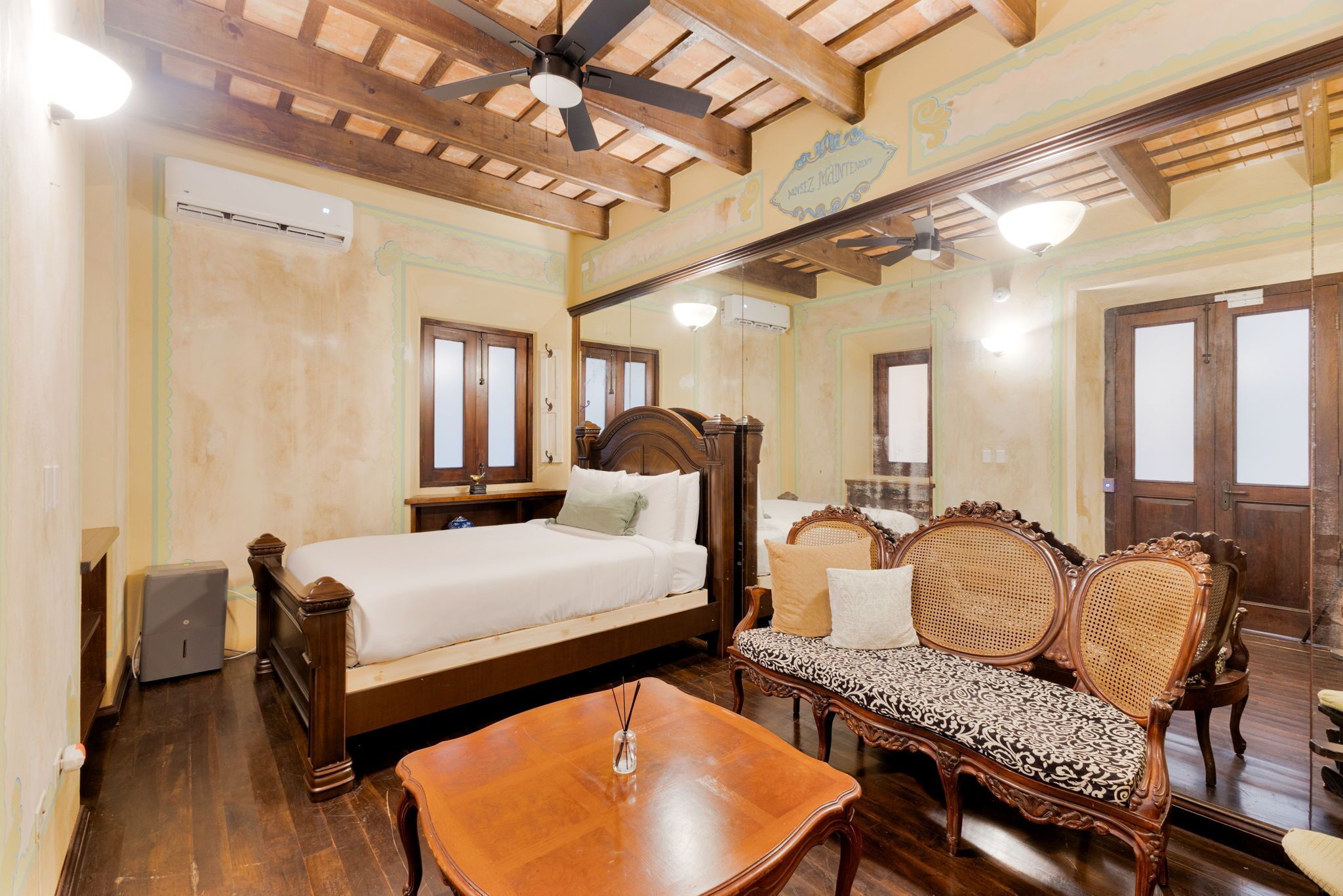 A room with a bed, a wooden table, a bench, and a ceiling fan.