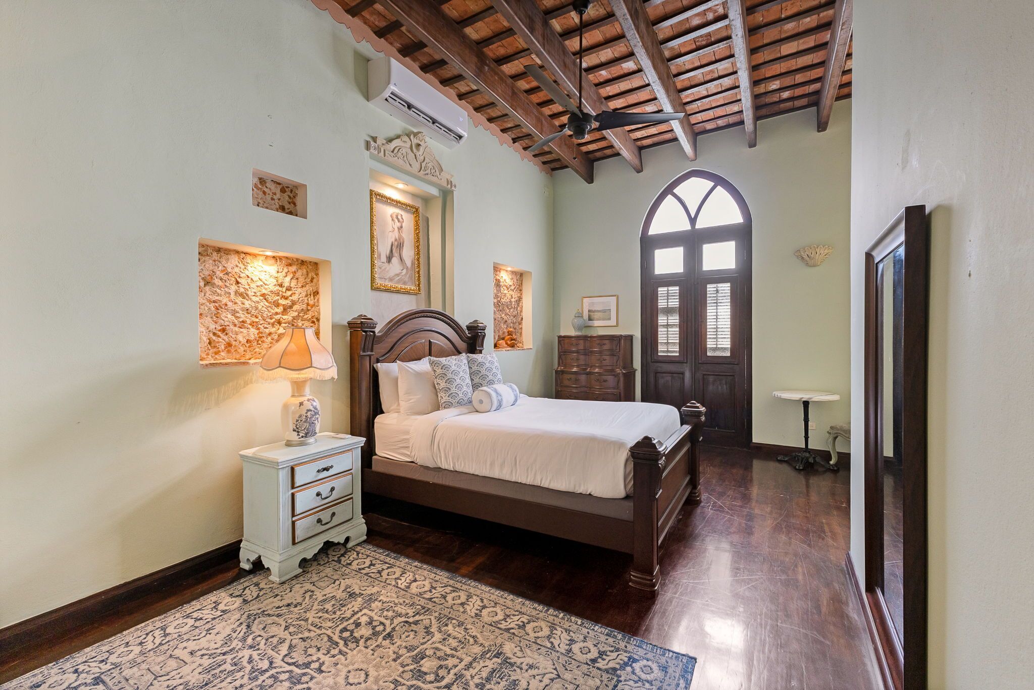 A bedroom with a bed, bedside table, lamp, and a large window.