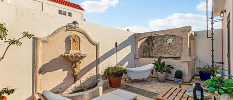 Une terrasse sur le toit avec une baignoire blanche, des chaises longues et des plantes en pot.
