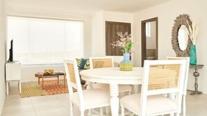 A dining area with a round white table, white upholstered chairs, and a vase with flowers.