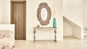 A room with a wooden door, a console table with a mirror, a vase, and a staircase.