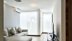 Ein modernes Wohnzimmer mit einer Couch, einem Flachbildfernseher und einer Glastür, die auf einen Balkon führt.