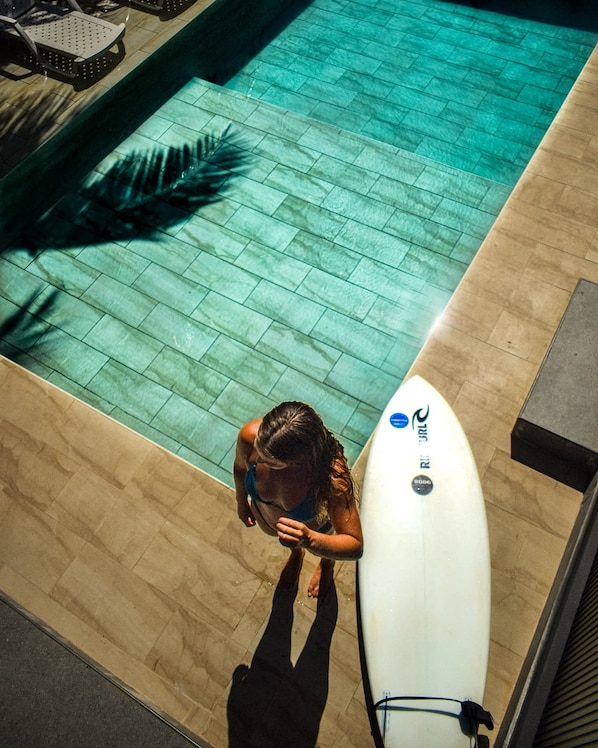 Una piscina con cubierta de azulejos y una tabla de surf apoyada al borde.