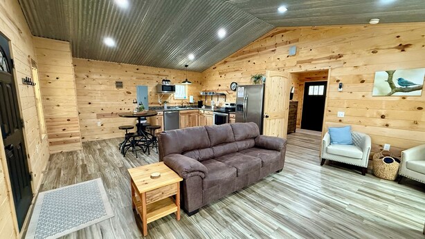 A cozy cabin interior with a wooden dining area, a kitchenette, a sofa, and a small table. - Bird House (Fort Payne)