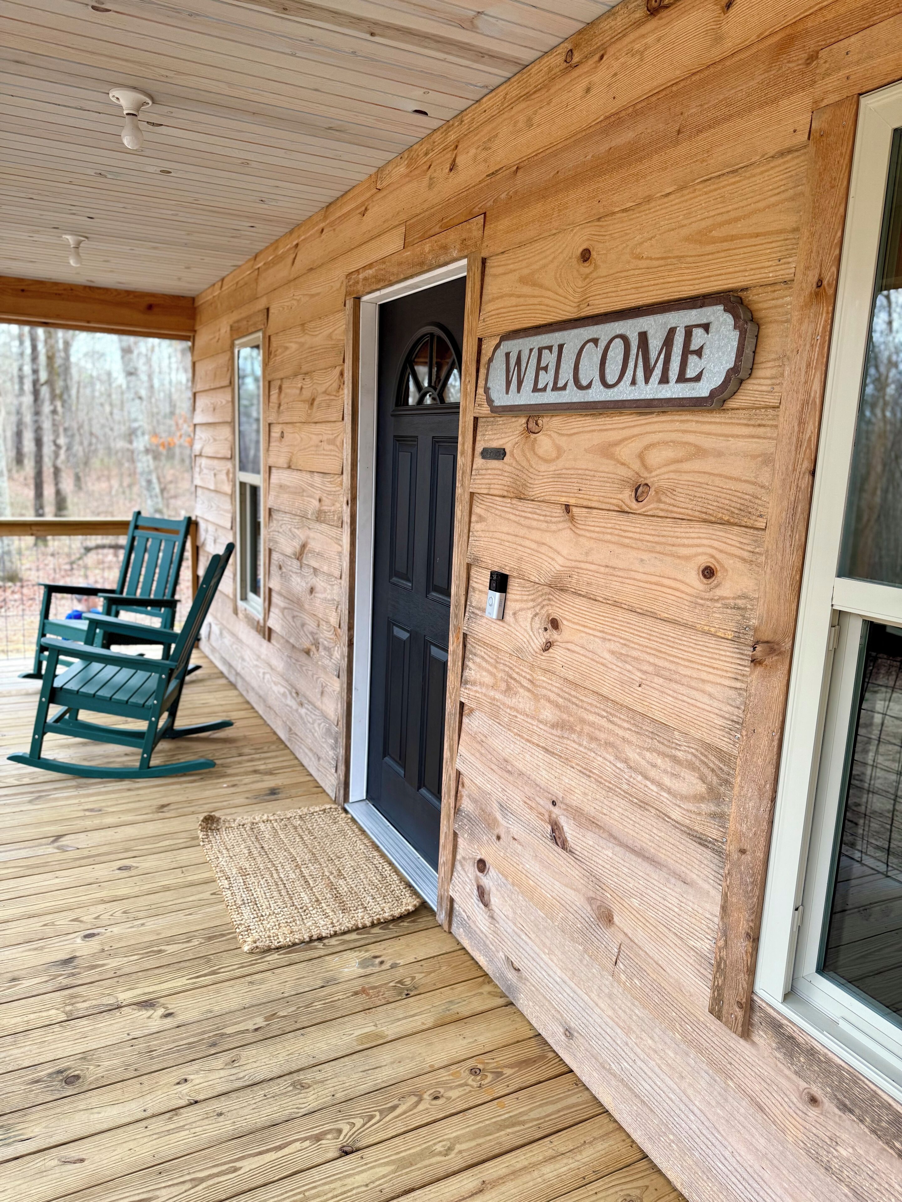 A wooden cabin with a welcome sign, a black door, and a rocking chair on the porch.
