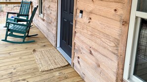 A wooden cabin with a welcome sign, a black door, and a rocking chair on the porch. - Bird House (Fort Payne)