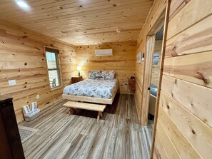 Ein Schlafzimmer einer Holzhütte mit einem Bett, Nachttisch, Lampe und einem Fenster.