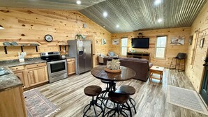 A wooden interior with a kitchen, dining area, and living room, featuring a refrigerator, stove, and TV. - Bird House (Fort Payne)
