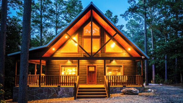 A log cabin with a stone foundation, wooden exterior, and a porch with railings.