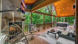 A wooden deck with a stone fireplace, a hanging chair, and a sofa with cushions.