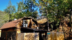 A rustic wooden cabin with a metal roof, a large wheel, and a wooden fence.