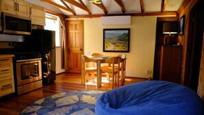 A kitchen with wooden cabinets, a microwave, a stove, and a refrigerator. There is a dining table with chairs and a blue bean bag chair.