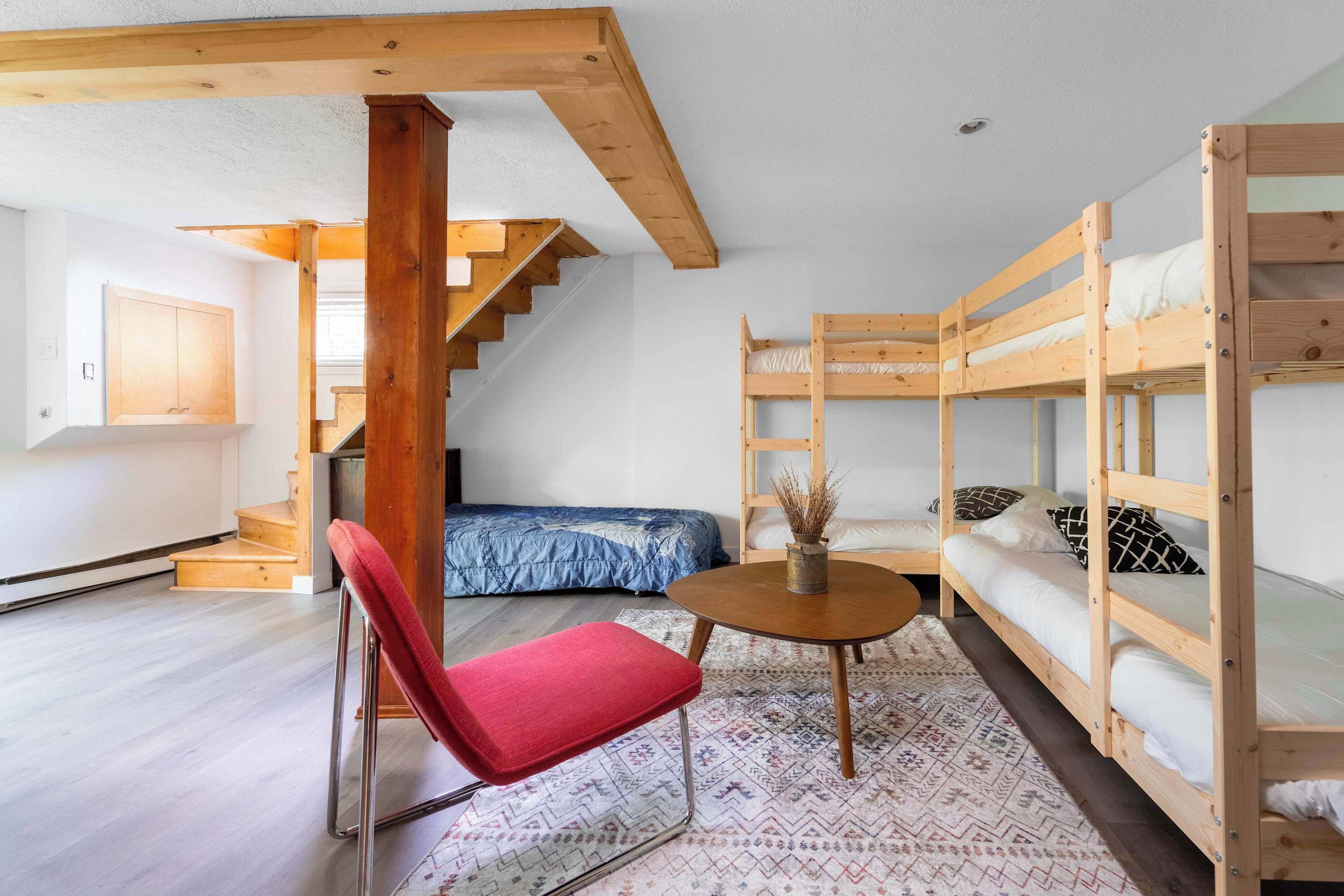 Une pièce avec des lits superposés, une chaise rouge, une petite table ronde et un escalier.
