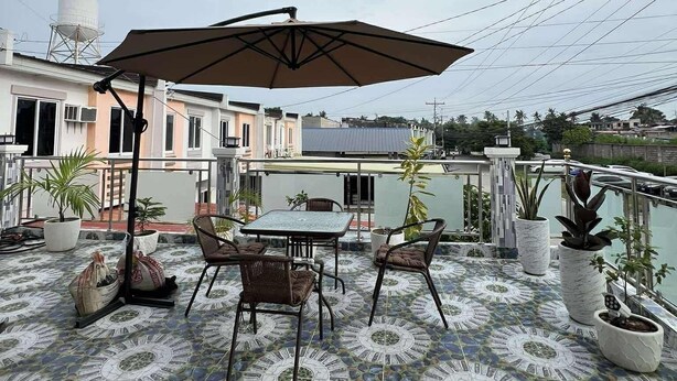 A rooftop terrace with a tiled floor, a table with chairs, an umbrella, and potted plants. - Charming Bed & Breakfast Room #1 with WiFi and AC in Delightful Compostela Cebu (Compostela)