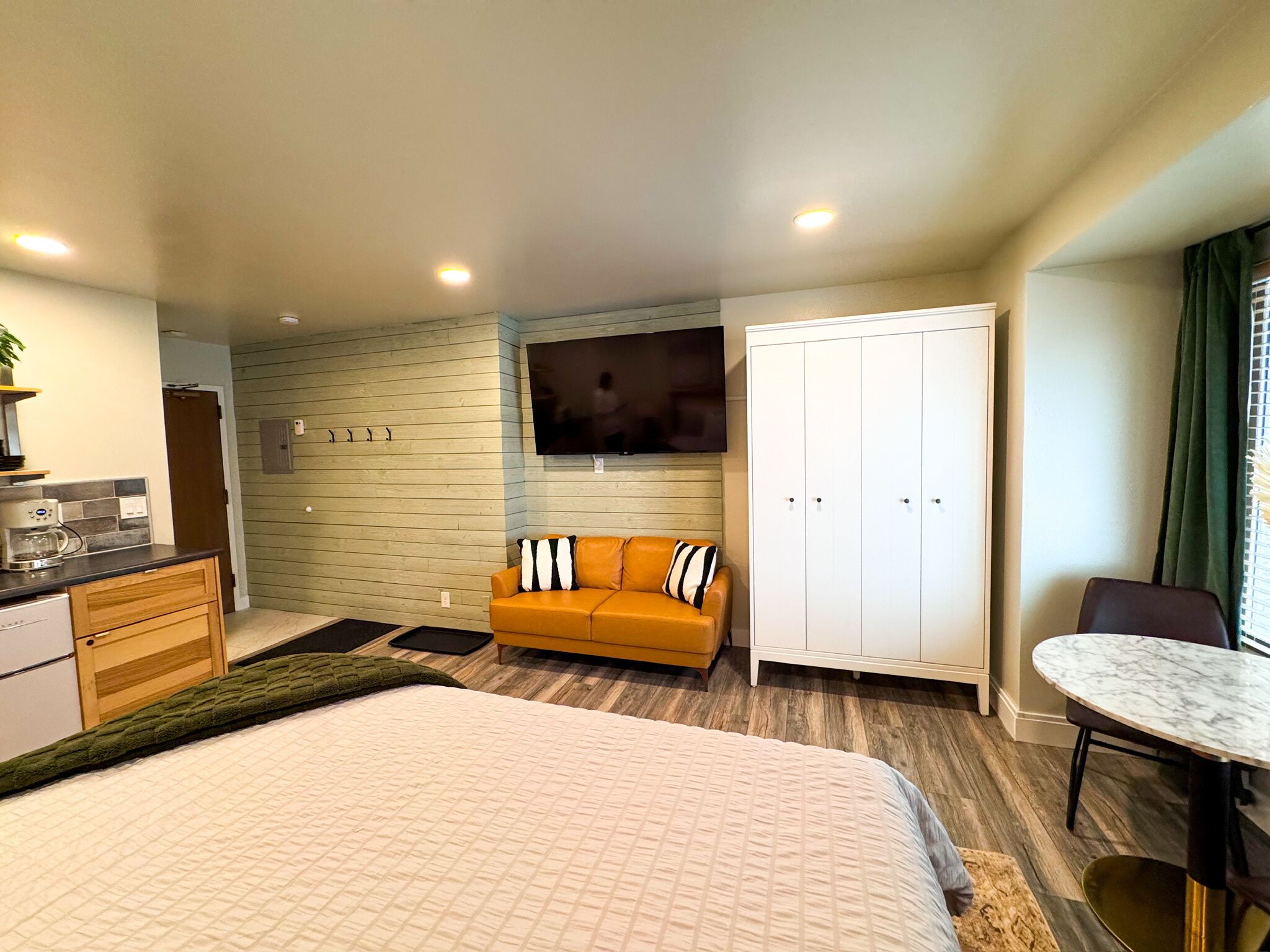 A modern hotel room with a large bed, a sofa, a TV, a wardrobe, and a dining table.