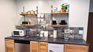 Une cuisine compacte équipée d’un four à micro-ondes, d’un grille-pain, d’une machine à café et d’un lave-vaisselle. Elle comprend des placards en bois et un petit réfrigérateur.