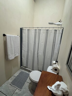 A small bathroom with a toilet, a shower curtain with a leaf pattern, a towel hanging on the wall, and a patterned rug on the floor.