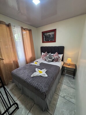 A neatly made bed with a grey blanket, two pillows with a leaf pattern, and a framed picture on the wall.