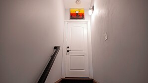 A narrow hallway with a white door at the end, a carpeted staircase, and a painting above the door. - Charming 3-bedroom apartment with WiFi, AC in lovely Leominster (Leominster)