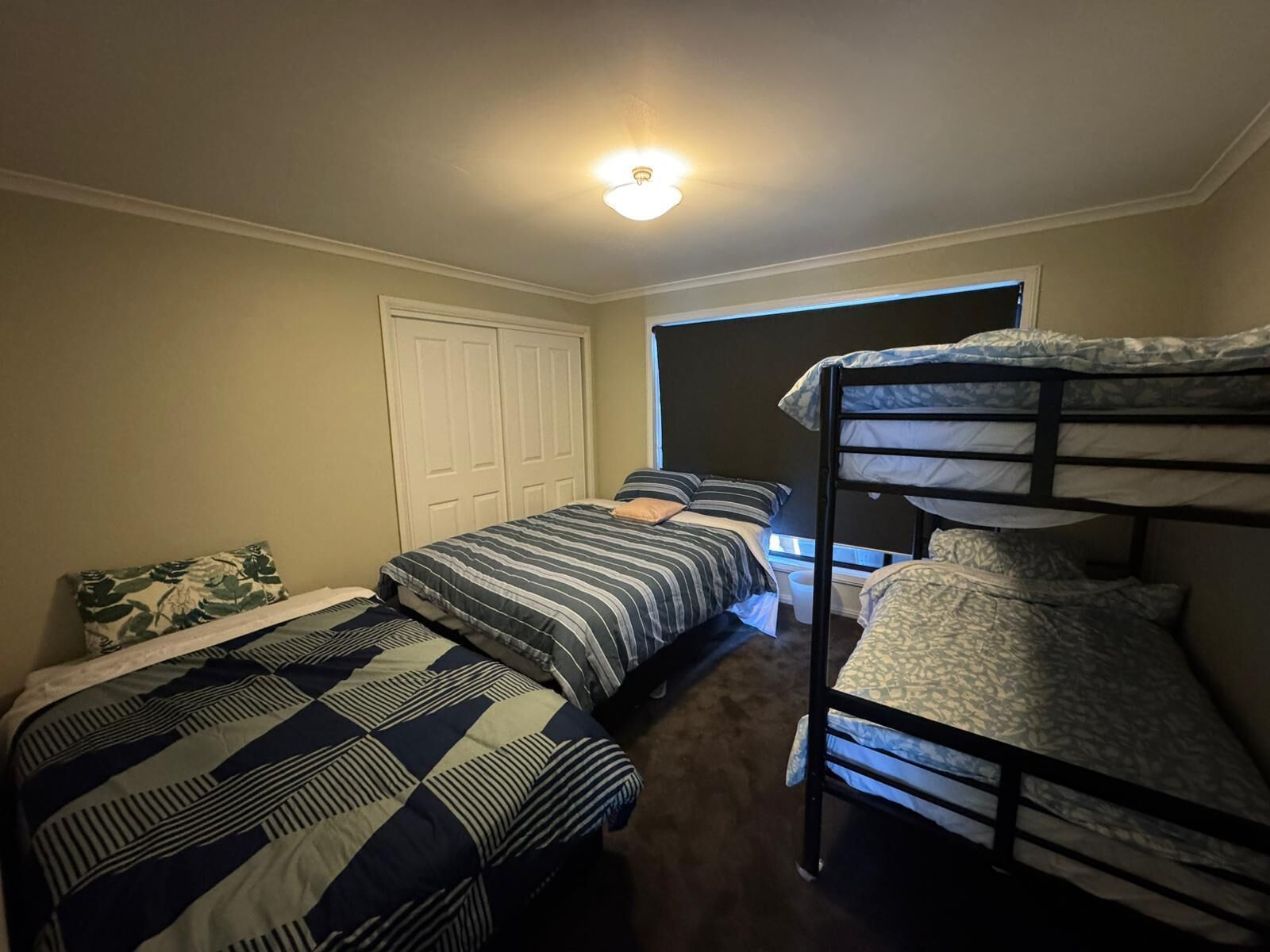Habitación tipo dormitorio con dos camas individuales, una litera, un armario y una ventana.