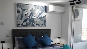 A modern bedroom with a large bed, a headboard, and a wall-mounted air conditioning unit.