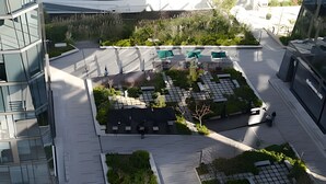 An aerial view of a modern urban plaza with geometric landscaping, seating areas, and a mix of greenery and paved surfaces.