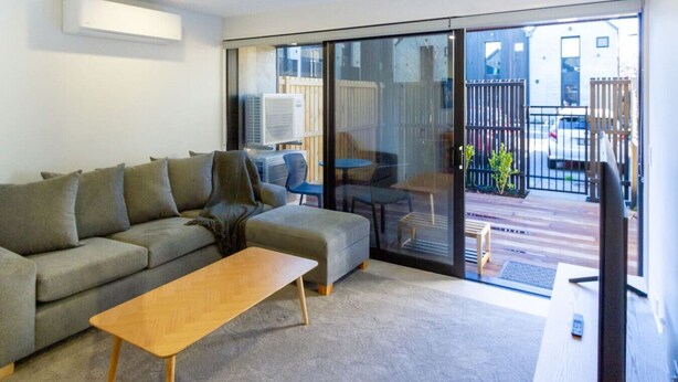 A modern living room with a grey sofa, a wooden coffee table, and a TV on a stand.