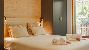 Une chambre à coucher avec une tête de lit en bois, un lit recouvert de draps blancs, une armoire sombre et une fenêtre donnant sur un paysage verdoyant.