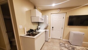 A compact kitchen with a sink, stove, and microwave. A door and a small trash bin are visible. - Modern 1BR Studio in Safe Alexandria Neighborhood , Near Metro & Dining. (Alexandria)