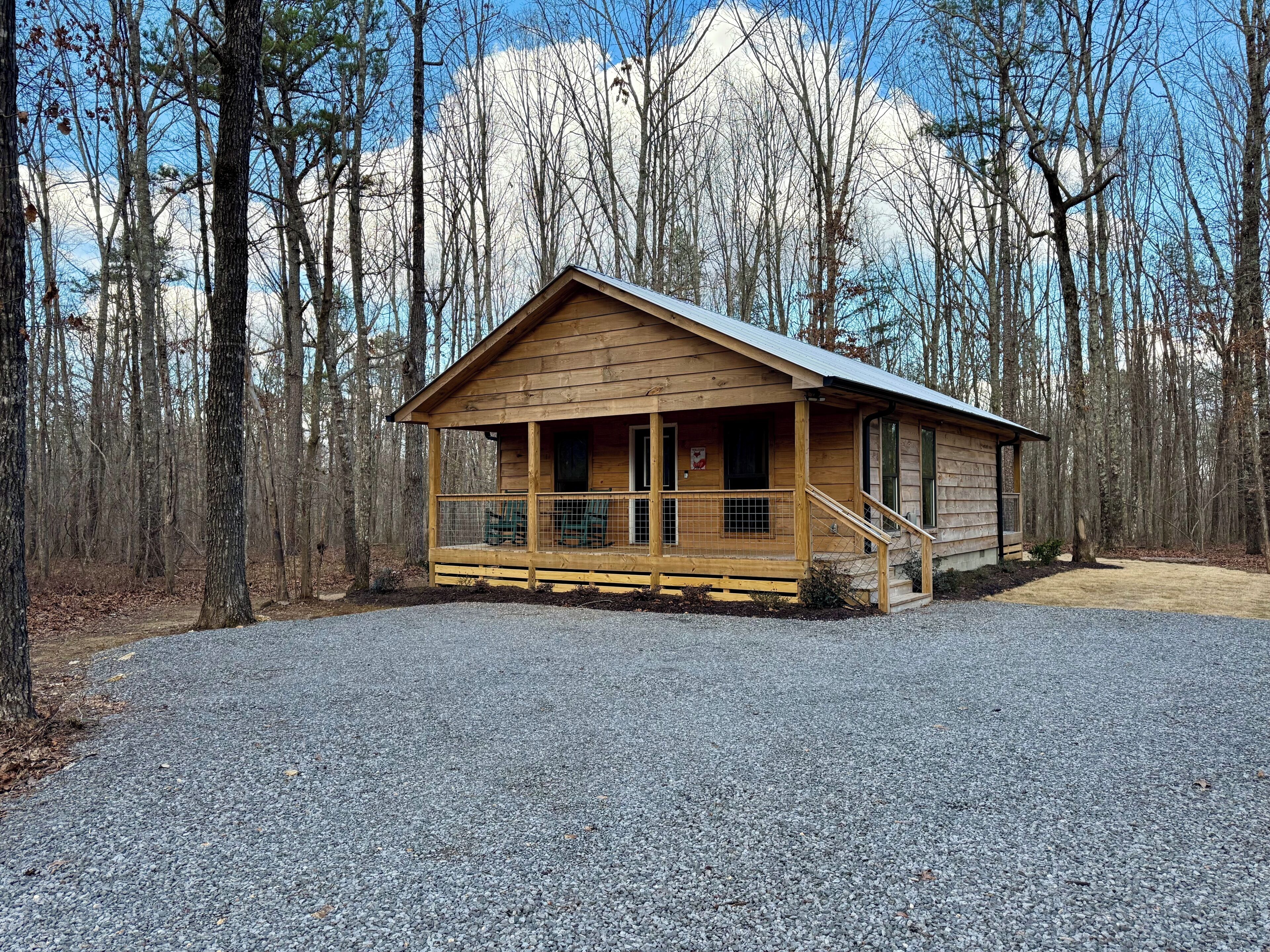 A wooden cabin with a porch, a staircase, and a gravel driveway.