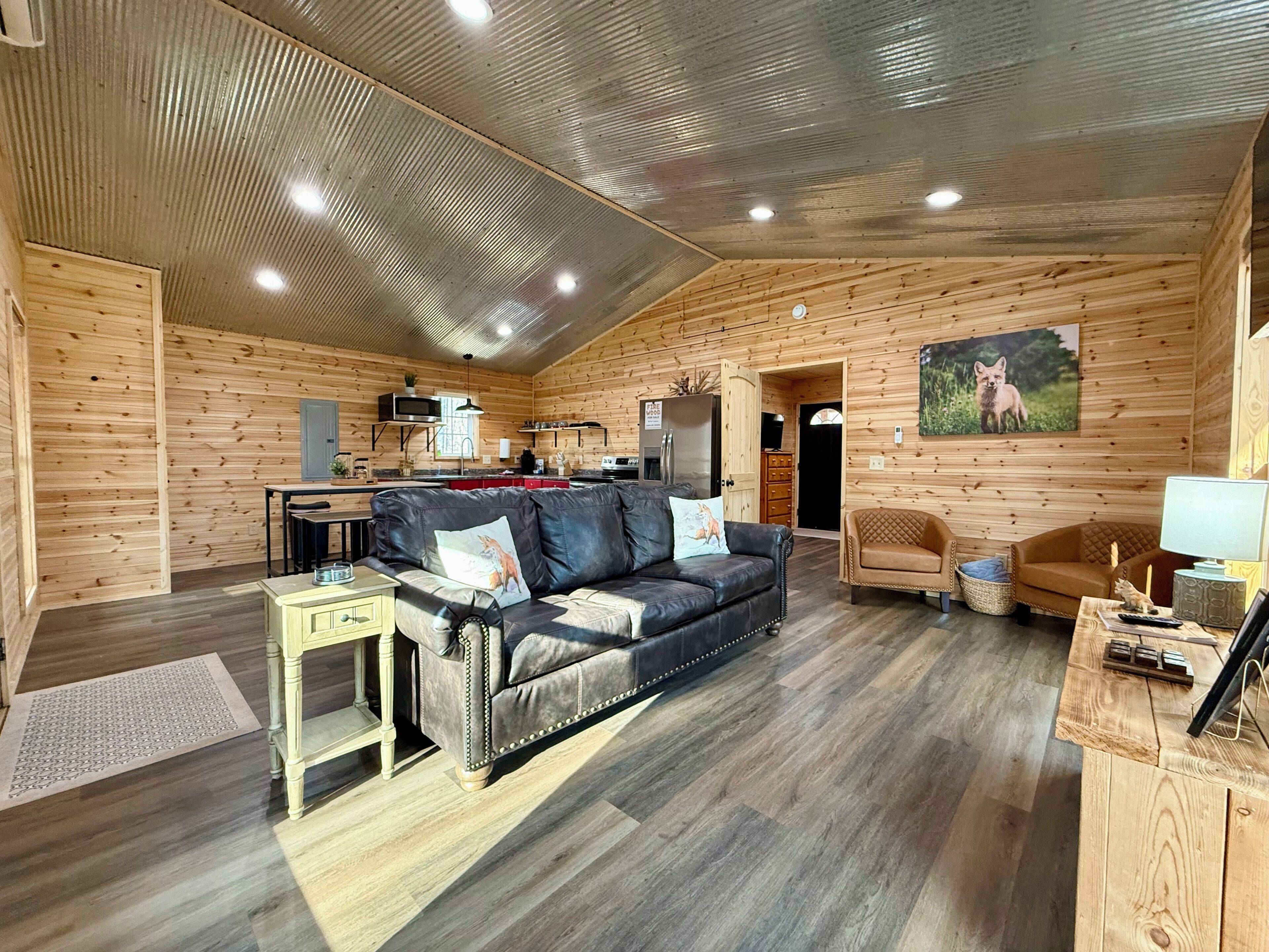 A spacious living area with a wooden interior, a leather sofa, a dining table, and a kitchen in the background.