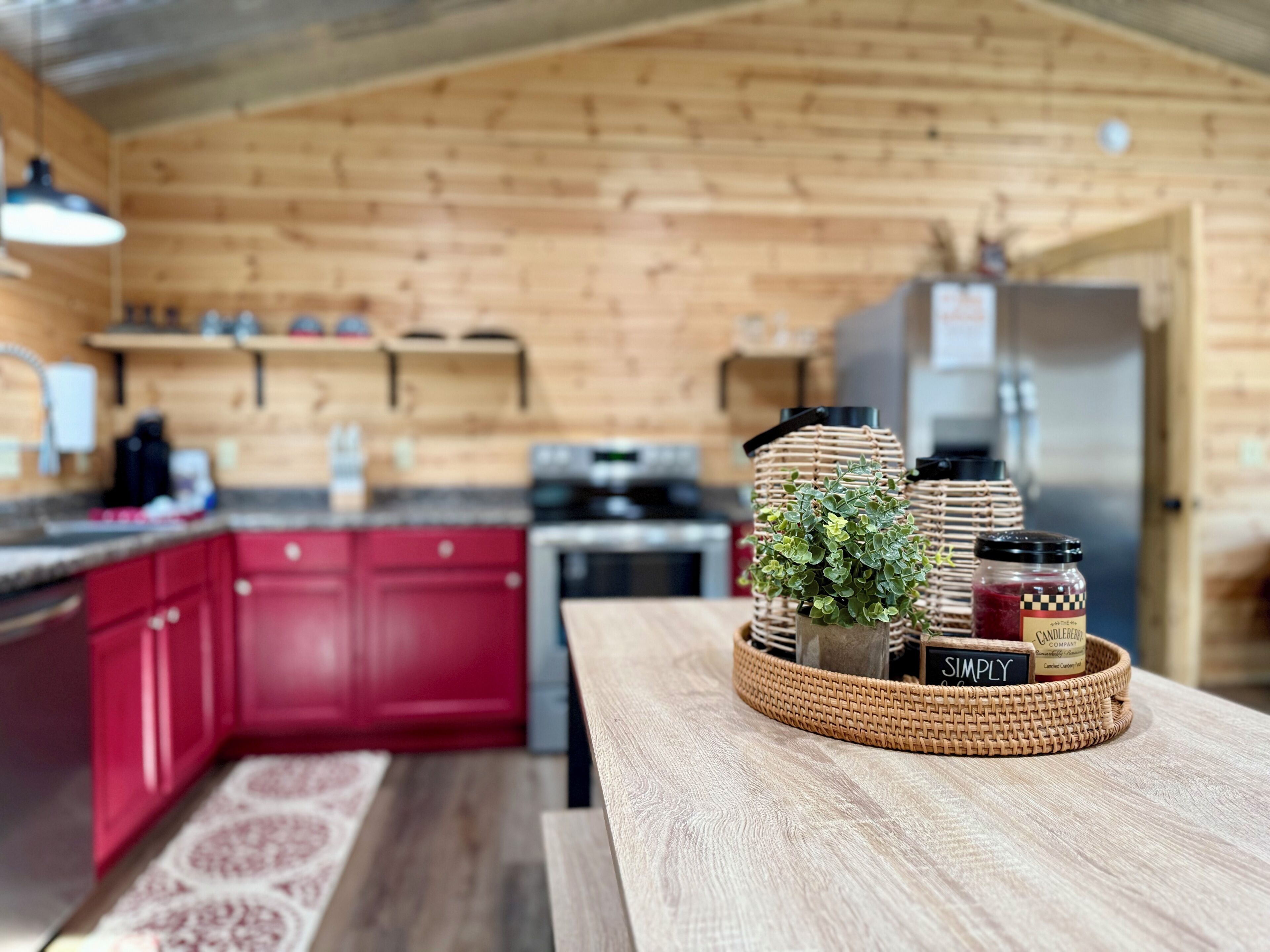 A kitchen with wooden walls, a red countertop, and a woven basket with jars and a plant.