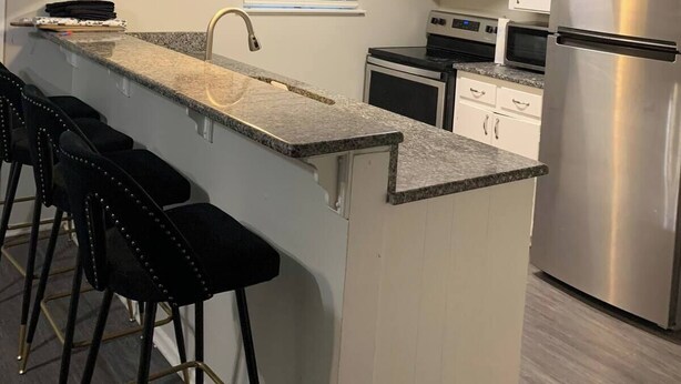 Una cocina moderna con encimera de granito, electrodomésticos de acero inoxidable y taburetes de bar.