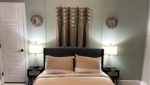 A bedroom with a bed, two bedside tables, two wall sconces, and a decorative wall hanging. - Peach Place (McGill)