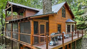 A log cabin with a deck, large windows, and a stone chimney. - Walk to Lake Blue Ridge | Hot Tub + Fire Pit (Morganton)