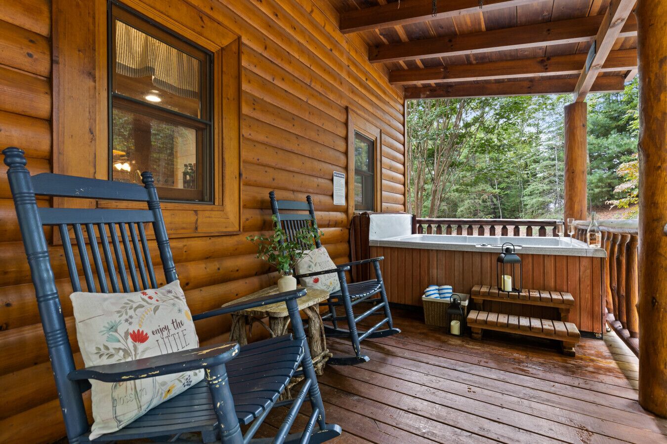 A wooden cabin with a porch featuring rocking chairs, a small table, and a hot tub.