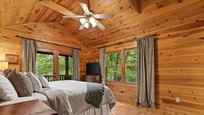 A wooden cabin bedroom with a bed, a nightstand, a TV, and a ceiling fan. - Walk to Lake Blue Ridge | Hot Tub + Fire Pit (Morganton)
