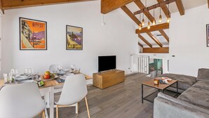 A spacious living area with a dining table set for two, a sofa, and a television.