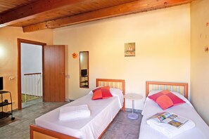 A hotel room with two single beds, a small round table, a TV, and a door leading to a balcony.