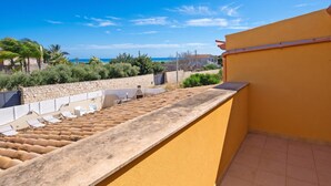 Un balcon avec vue sur la mer, un mur en pierre et une rangée de chaises longues.