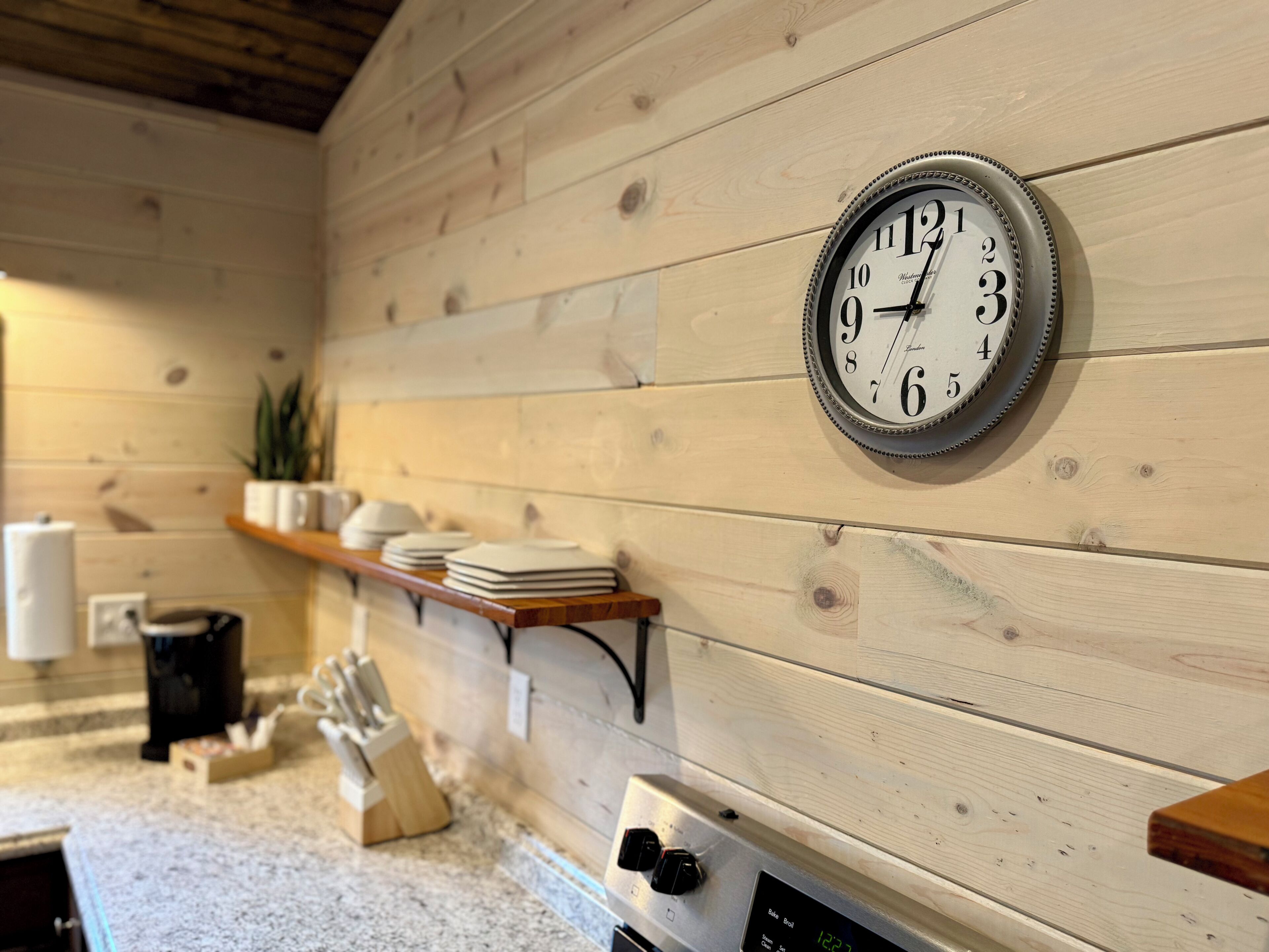 A kitchen with wooden walls, a clock, a coffee maker, and a knife block.